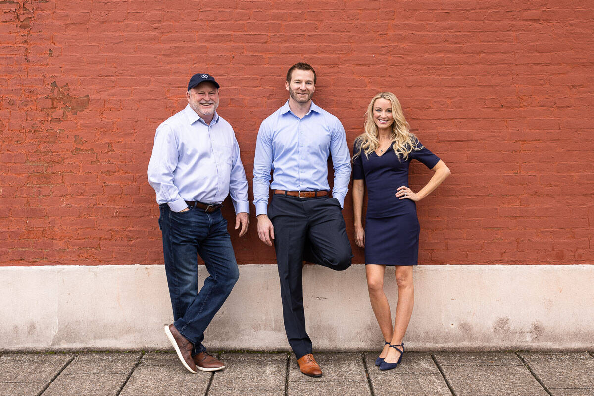 three people lean against orange brick painted wall